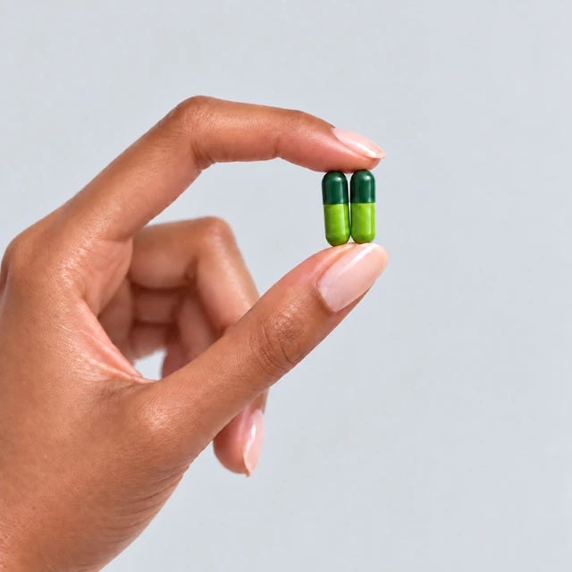 A hand lightly holds two green capsules upright side by side.